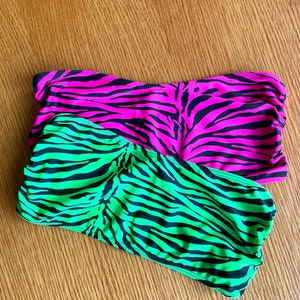 May include: Two strapless tops with a zebra print pattern. One top is pink with black stripes and the other is green with black stripes.