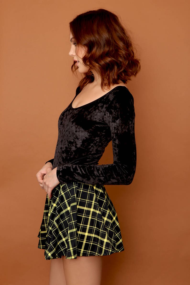 May include: A black long-sleeved velvet top with a scoop neck paired with a black and yellow plaid skirt.