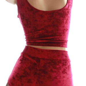 May include: A burgundy velvet two-piece set, comprising a crop top and high-waisted shorts. The fabric has a textured finish. The top features a scoop neckline and the shorts have a wide waistband. The outfit is displayed on a mannequin.