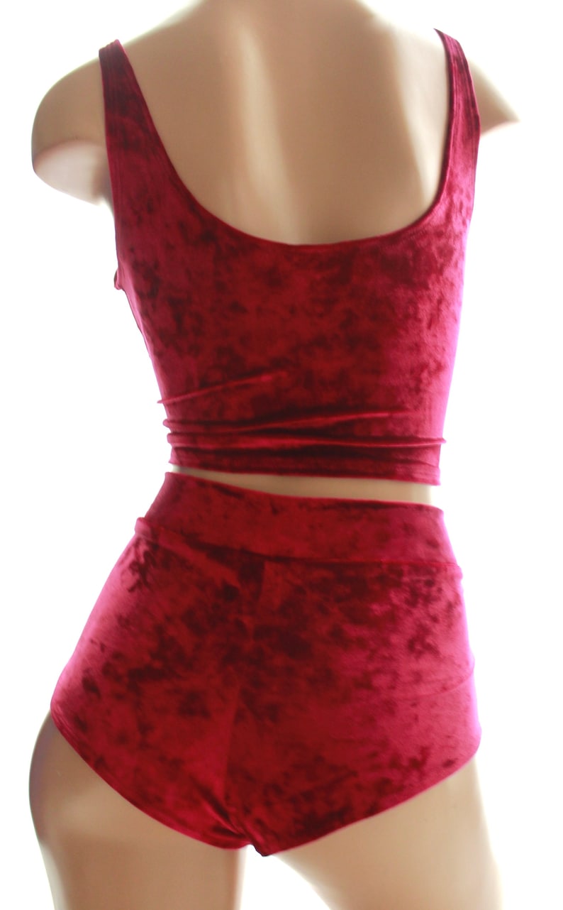 May include: A burgundy velvet two-piece set, comprising a crop top and high-waisted shorts. The fabric has a textured finish. The top features a scoop neckline and the shorts have a wide waistband. The outfit is displayed on a mannequin.
