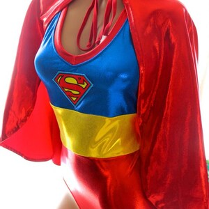 K&ouml;nnte beinhalten: Ein Superman-Kost&uuml;m in Rot, Blau und Gelb. Das Kost&uuml;m besteht aus einem roten Umhang, einem blauen Oberteil mit dem Superman-Logo, einem gelben G&uuml;rtel und einer roten Hose. Das Kost&uuml;m ist aus gl&auml;nzendem, metallischem Stoff gefertigt.
