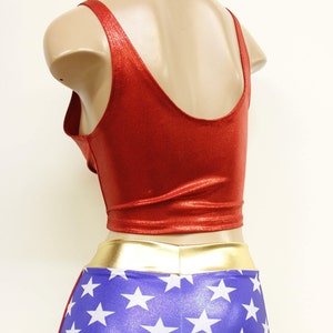 Pode incluir: Traje de spandex vermelho e azul com um cinto dourado e estrelas brancas. A parte superior &eacute; um top curto sem mangas com decote redondo. A parte inferior &eacute; um short com padr&atilde;o de estrelas.