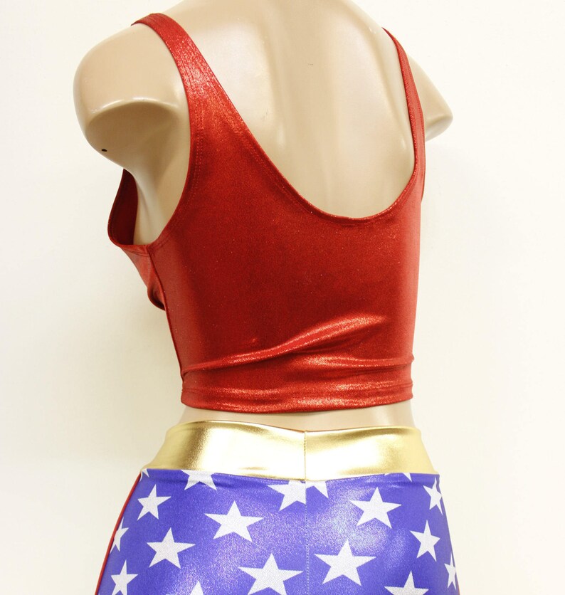 Pode incluir: Traje de spandex vermelho e azul com um cinto dourado e estrelas brancas. A parte superior &eacute; um top curto sem mangas com decote redondo. A parte inferior &eacute; um short com padr&atilde;o de estrelas.