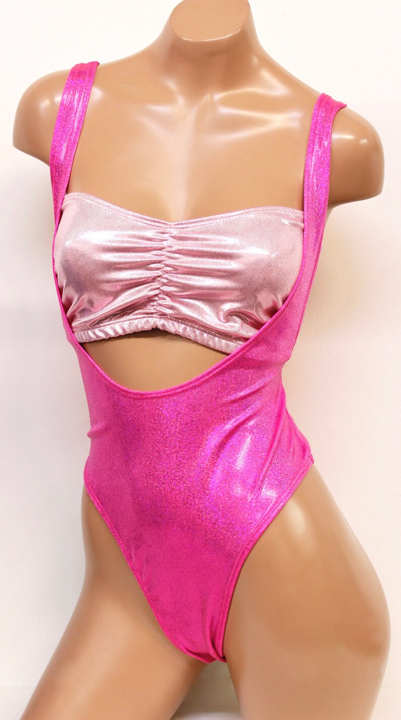 May include: A pink and silver sparkly leotard with a matching halter top. The leotard has a cut-out design at the front and a high leg cut.