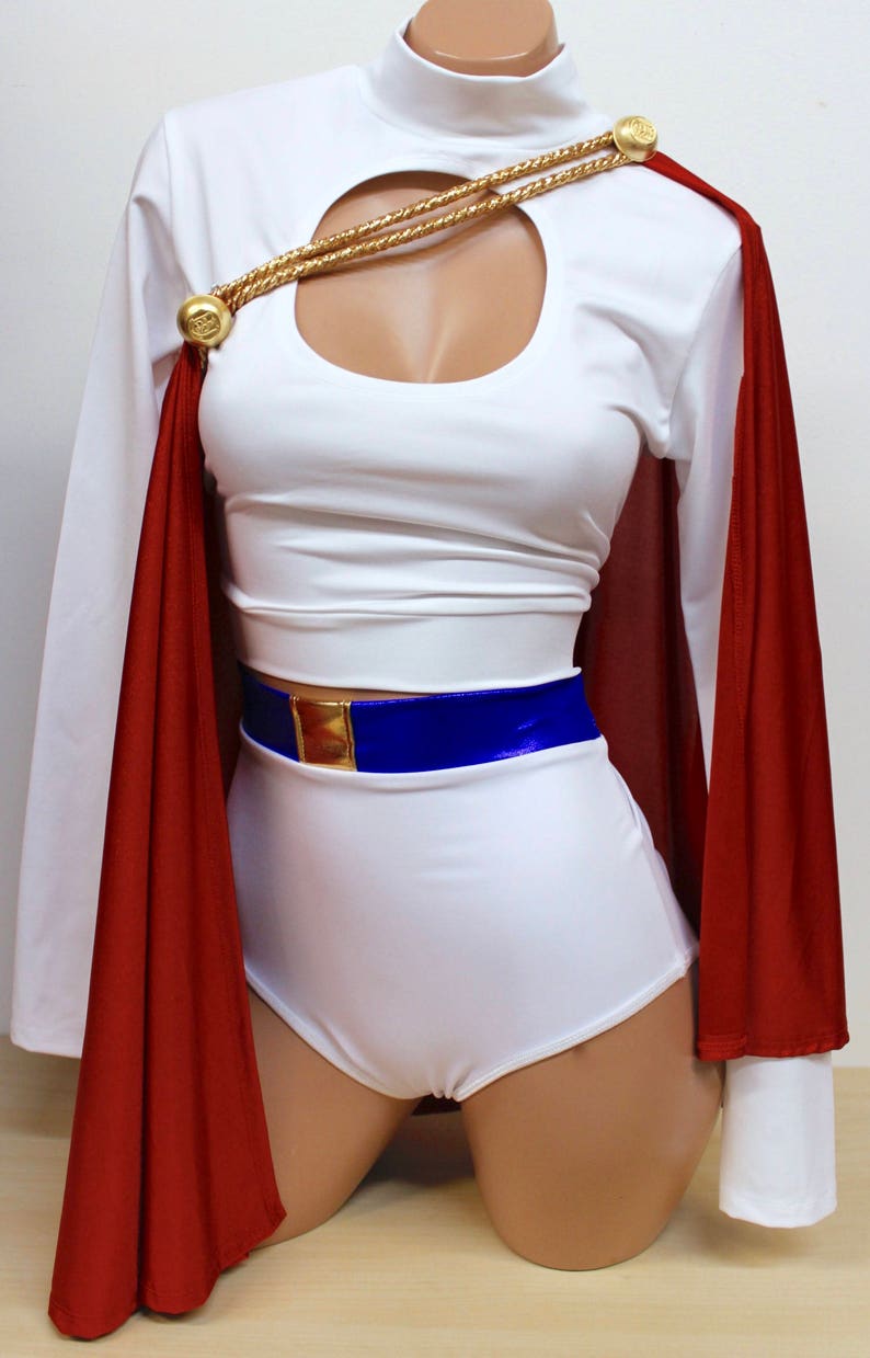 Puede incluir: Top blanco corto con un escote de ojo de cerradura y un detalle de cadena dorada. El top se combina con pantalones cortos blancos y una capa roja. Un cintur&oacute;n azul con una hebilla dorada completa el look.