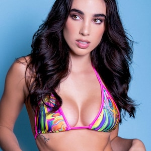 May include: A colorful bikini top with a vibrant, swirling pattern in shades of pink, yellow, green, and blue. The top has a pink trim and is set against a light blue background. The overall style is summery and playful.