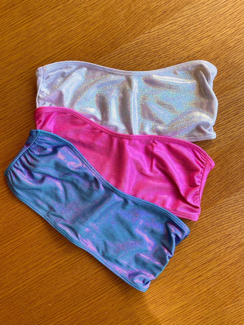 May include: Three tube tops in different colors: silver, pink, and blue. The tube tops are made of a shiny, iridescent fabric.