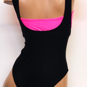May include: Black swimsuit with a pink lining. The swimsuit has a scoop neck and a racerback style.