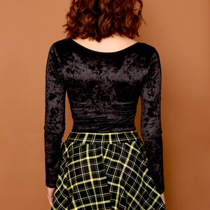 May include: A black long-sleeved velvet top with a scoop neck paired with a black and yellow plaid skirt.