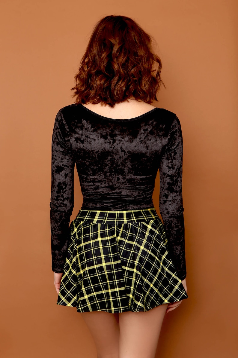 May include: A black long-sleeved velvet top with a scoop neck paired with a black and yellow plaid skirt.