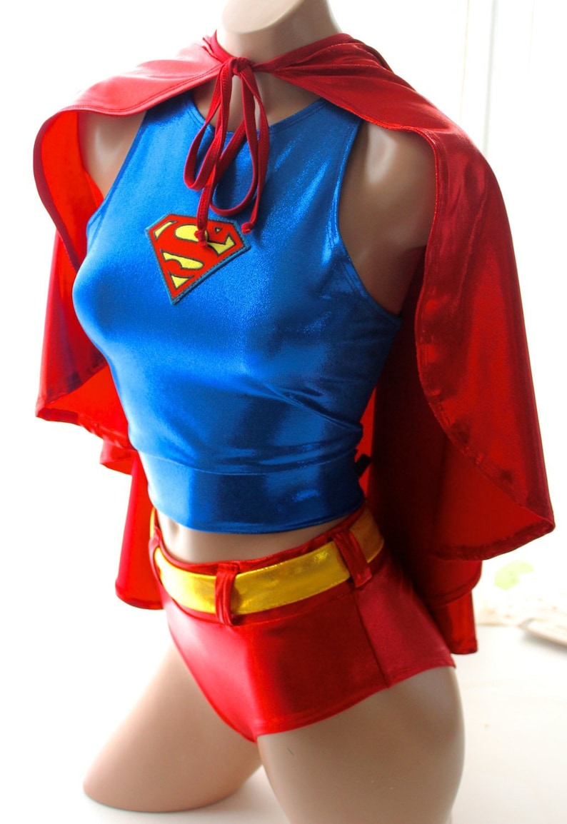 K&ouml;nnte beinhalten: Ein Superhelden-Kost&uuml;m mit einem blauen Oberteil mit Superman-Logo, roten Shorts, einem goldenen G&uuml;rtel und einem roten Umhang. Das Kost&uuml;m besteht aus gl&auml;nzendem Material und wird auf einer Schaufensterpuppe pr&auml;sentiert.