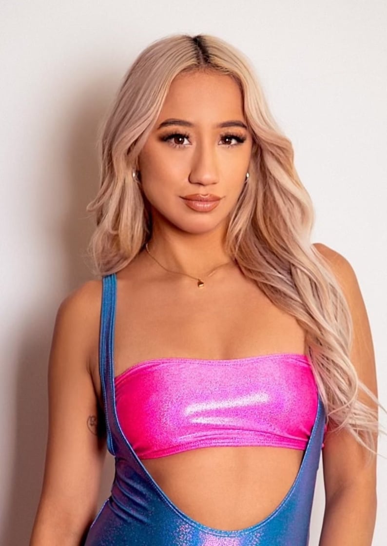 May include: A woman with long blonde hair is wearing a pink and blue iridescent halter top. The top has a bandeau style top and thin straps.
