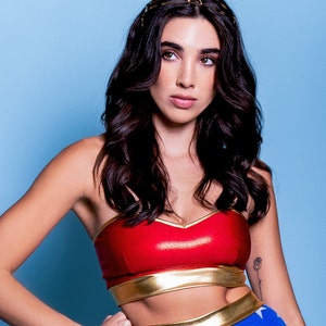 May include: A woman wearing a red and gold Wonder Woman costume with a star-shaped headband. The costume features a red bustier with a gold band, a blue skirt with white stars, and a gold belt with a rope detail.