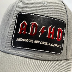 May include: Gray baseball cap with a black leather patch that says "ADHD" in red letters with a lightning bolt and the text "Highway to, Hey Look, A Squirrel".