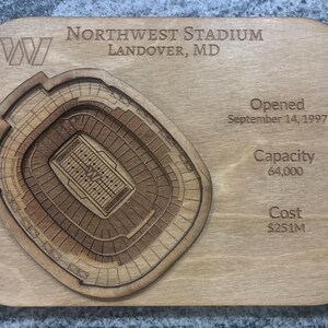 May include: A wooden plaque with a laser-cut stadium design. The text reads "Northwest Stadium, Landover, MD," with details: "Opened September 14, 1997," "Capacity 64,000," and "Cost $251M." The stadium model is intricately layered and detailed.