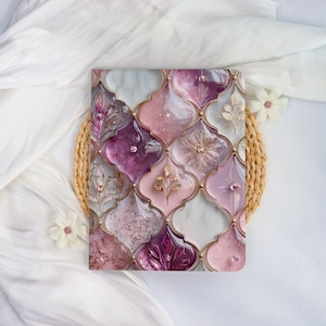May include: A square decorative object with a mosaic design in pink, purple, and white, framed with gold-coloured trim. The mosaic features floral and geometric patterns, with embedded crystals. The object rests on a woven, circular base.