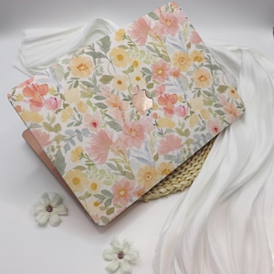 May include: A laptop with a floral design. The case features a watercolour pattern of pink, yellow, and peach flowers with green leaves on a white background. The laptop is open, revealing a rose gold interior.