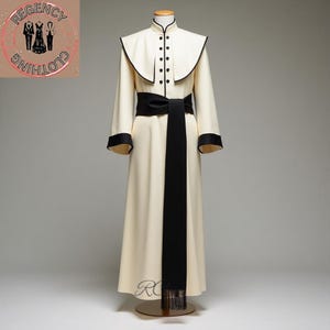 Może przedstawiać: Kremowy długi płaszcz z czarnym pasem i wykończeniem, prezentowany na manekinie. Płaszcz posiada wysoki kołnierz, czarne guziki i kołnierz w kształcie peleryny. Czarny pas rozciąga się z przodu, kończąc się frędzlami.