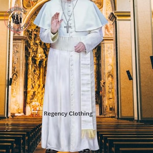 Może przedstawiać: Biała sutanna z długim białym pasem i rzędem guzików z przodu. Sutannę nosi osoba stojąca w kościele. Tekst "Regency Clothing" jest widoczny na dole obrazu.