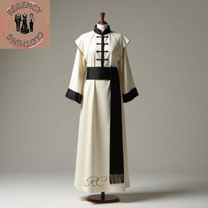 Może przedstawiać: Kremowa szata z długimi rękawami z czarnymi wykończeniami i akcentami. Szata posiada kołnierz mandaryński, czarne zapięcia żabkowe i szeroki czarny pas. Na dole szaty wyhaftowano litery "RC". Logo Regency Clothing znajduje się w lewym górnym rogu.