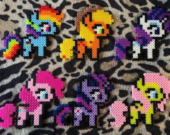 May include: A set of seven colorful My Little Pony characters made with perler beads. The ponies are all different colors and have different designs.