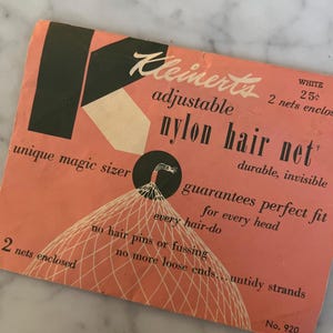 Puede incluir: Embalaje vintage de redecilla para el cabello de nailon Kleinert's. La tarjeta de color melocotón presenta texto y gráficos en blanco y negro, incluidas las palabras "adjustable nylon hair net" y "guarantees perfect fit". El embalaje también indica "2 redes incluidas".