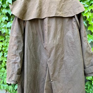 May include: A brown, long coat with a cape-like collar. The coat has a button closure and is made of a durable, possibly waxed, material. The coat is designed to provide protection from the elements.