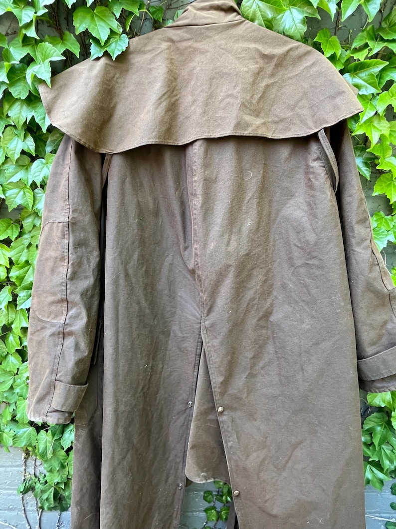 May include: A brown, long coat with a cape-like collar. The coat has a button closure and is made of a durable, possibly waxed, material. The coat is designed to provide protection from the elements.