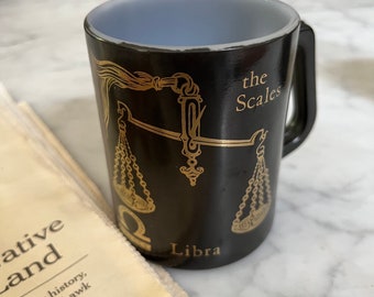 Pode incluir: Caneca de cerâmica preta com um design dourado de uma balança e as palavras "Libra" e "the Scales".