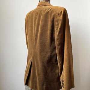 Op de afbeelding: Bruine corduroy blazer met een gekerfde revers en drie knopen op elke manchet. De blazer wordt getoond op een mannequin, met de achterkant en het zijprofiel. De stof heeft een geribbelde textuur.