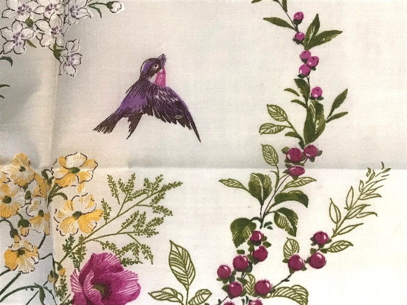 Pu&ograve; includere: Un tessuto bianco con un motivo floreale. Il motivo comprende fiori viola, fiori gialli, foglie verdi e un uccello viola.