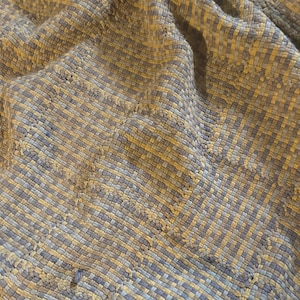 Puede incluir: Primer plano de una tela tejida con un patrón texturizado. La tela es una mezcla de colores marrón claro y gris.