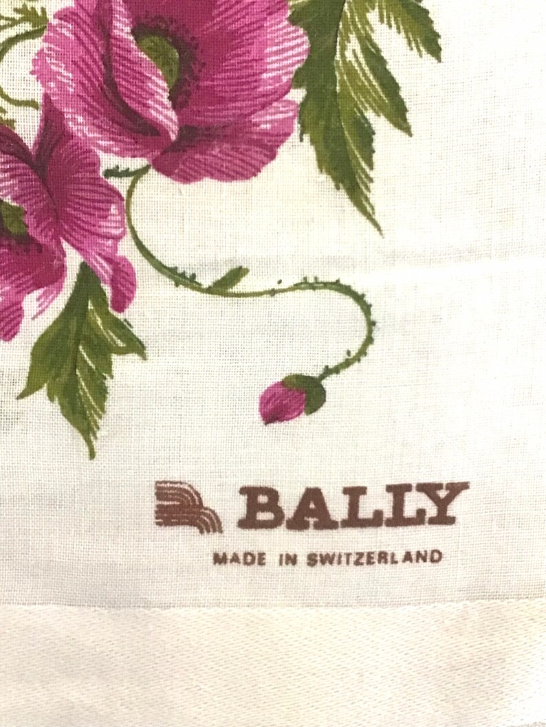 Pu&ograve; includere: Un tessuto bianco con un motivo floreale rosa e un logo Bally marrone con il testo "Made in Switzerland".