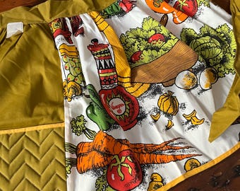 Könnte beinhalten: Eine vintage grüne und weiße Küchenschürze mit einem bunten Gemüseprint. Die Schürze hat eine große Tasche auf der Vorderseite und einen gelben Saum.