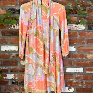 May include: A long-sleeved dress with a pink, orange, and yellow floral print. The dress has a tie at the neck and a loose fit.