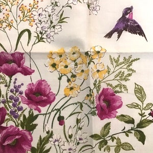 Pu&ograve; includere: Un tessuto bianco con un motivo floreale con papaveri rosa, fiori gialli e bianchi e foglie verdi. Un uccello viola sta volando nell'angolo in alto a destra dell'immagine.
