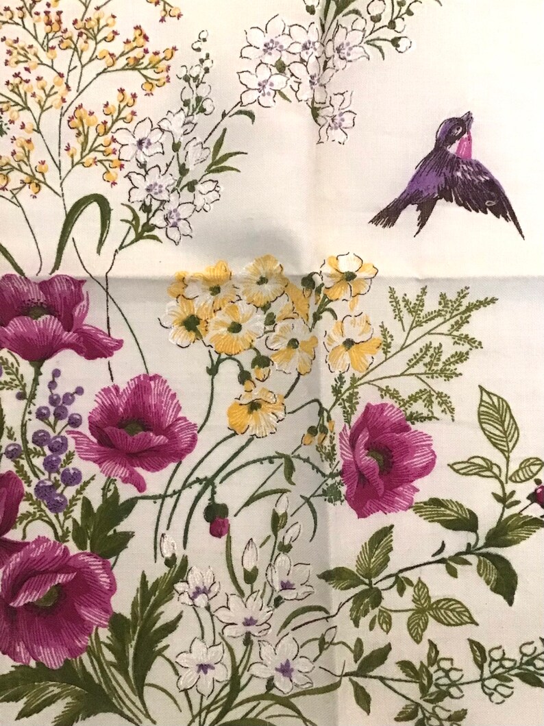 Pu&ograve; includere: Un tessuto bianco con un motivo floreale con papaveri rosa, fiori gialli e bianchi e foglie verdi. Un uccello viola sta volando nell'angolo in alto a destra dell'immagine.