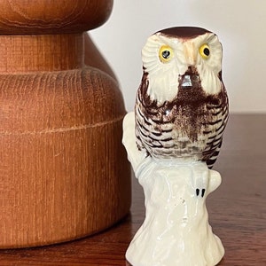 Könnte beinhalten: Eine Keramik-Eulenfigur mit braunen und weißen Markierungen, die auf einem weißen Baumstumpf sitzt. Die Eule hat gelbe Augen und einen braunen Schnabel.
