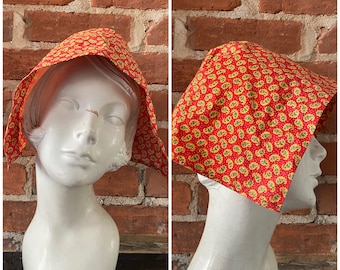 Puede incluir: Un cubrecabezas de tela con estampado rojo y amarillo, usado en una cabeza de maniquí blanca. La tela tiene un diseño paisley.