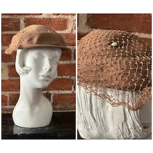 Könnte beinhalten: Ein brauner Filzhut mit einem braunen Netzschleier und einem Perlenakzent. Der Hut sitzt auf einem weißen Mannequin-Kopf.