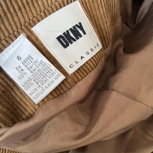 Op de afbeelding: Close-up van een bruin corduroy kledingstuk met een DKNY Classic label. Het label geeft aan dat het kledingstuk is gemaakt in Hong Kong en vermeldt de materialen rayon en polyester.
