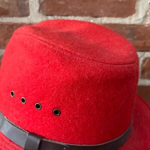 Puede incluir: Un sombrero fedora de fieltro rojo con una banda de cuero marr&oacute;n y cuatro ojales met&aacute;licos.