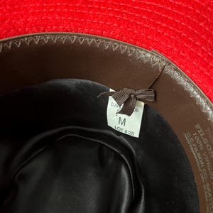 Puede incluir: El interior de un sombrero de fieltro marr&oacute;n con una banda de fieltro rojo. El sombrero est&aacute; etiquetado con "FILSON 100% VIRGIN WOOL C.C. FILSON CO. SEATTLE" y tiene una etiqueta de talla que dice "M LOT #25".