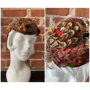 Könnte beinhalten: Ein Vintage-Hut aus Fasanenfedern in Braun-, Rot- und Grüntönen. Der Hut ist klein, rund und perfekt für einen Vintage- oder Retro-Look.