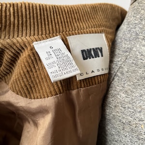 Op de afbeelding: Close-up van een bruin kledingstuk van corduroy met een DKNY Classic label. Het label bevat details over de stof, 100% rayon en polyester. Het kledingstuk is gemaakt in Hong Kong.