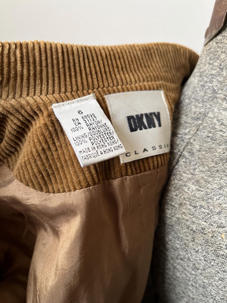 Op de afbeelding: Close-up van een bruin kledingstuk van corduroy met een DKNY Classic label. Het label bevat details over de stof, 100% rayon en polyester. Het kledingstuk is gemaakt in Hong Kong.