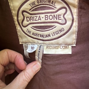May include: Close-up of a brown label from a riding coat. The label reads "THE ORIGINAL DRIZA-BONE THE AUSTRALIAN LEGEND." The size is 10, and the coat is made in Australia. The label also says "RIDING COAT."