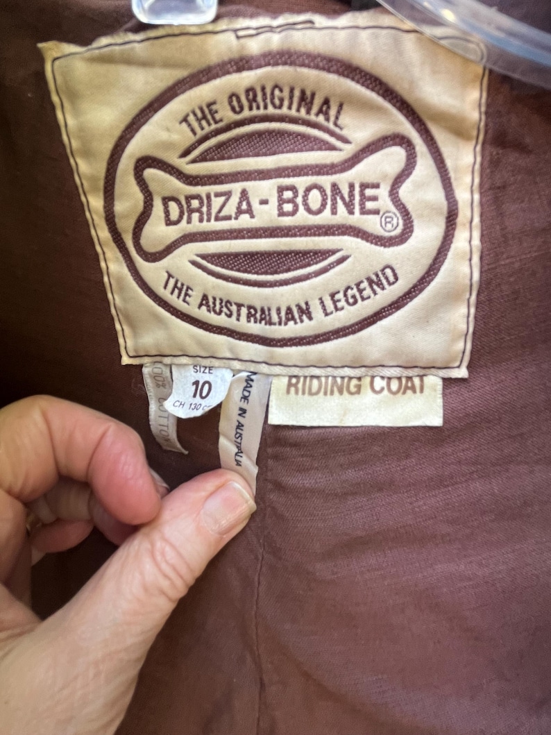 May include: Close-up of a brown label from a riding coat. The label reads "THE ORIGINAL DRIZA-BONE THE AUSTRALIAN LEGEND." The size is 10, and the coat is made in Australia. The label also says "RIDING COAT."