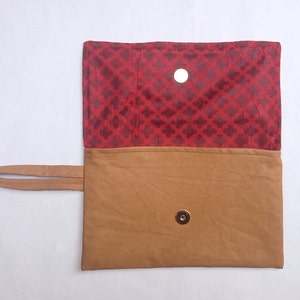 Puede incluir: Un clutch de cuero marr&oacute;n con un forro de tela roja y un cierre magn&eacute;tico. El clutch tiene una sola correa.