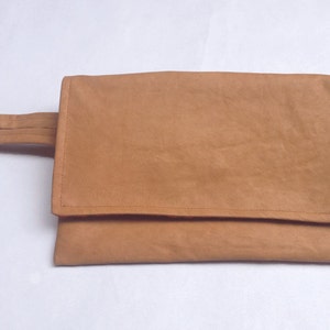 Puede incluir: Un clutch de ante marr&oacute;n con un asa de correa &uacute;nica.